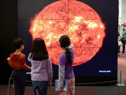A group of children pointing to a solar wall exhibit