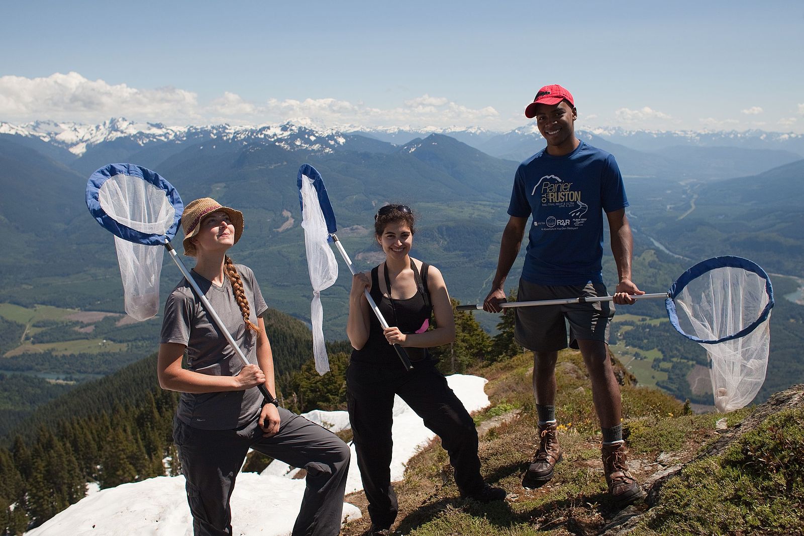 Three people with butterfly nets at a mountain vista.